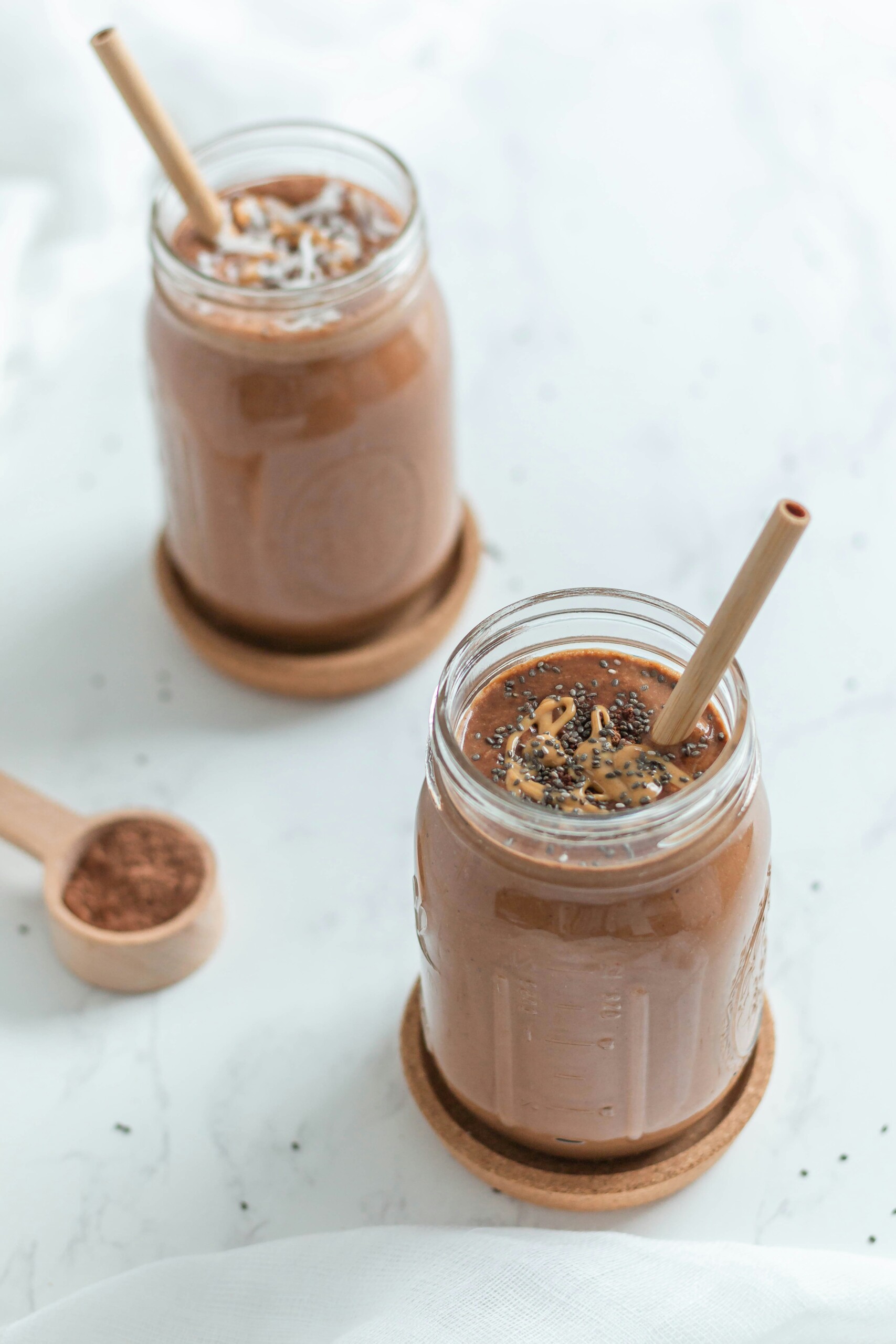 2 chocolat protein shakes in mason jars. One is toped with coconut and the other drizzeled with almond butter