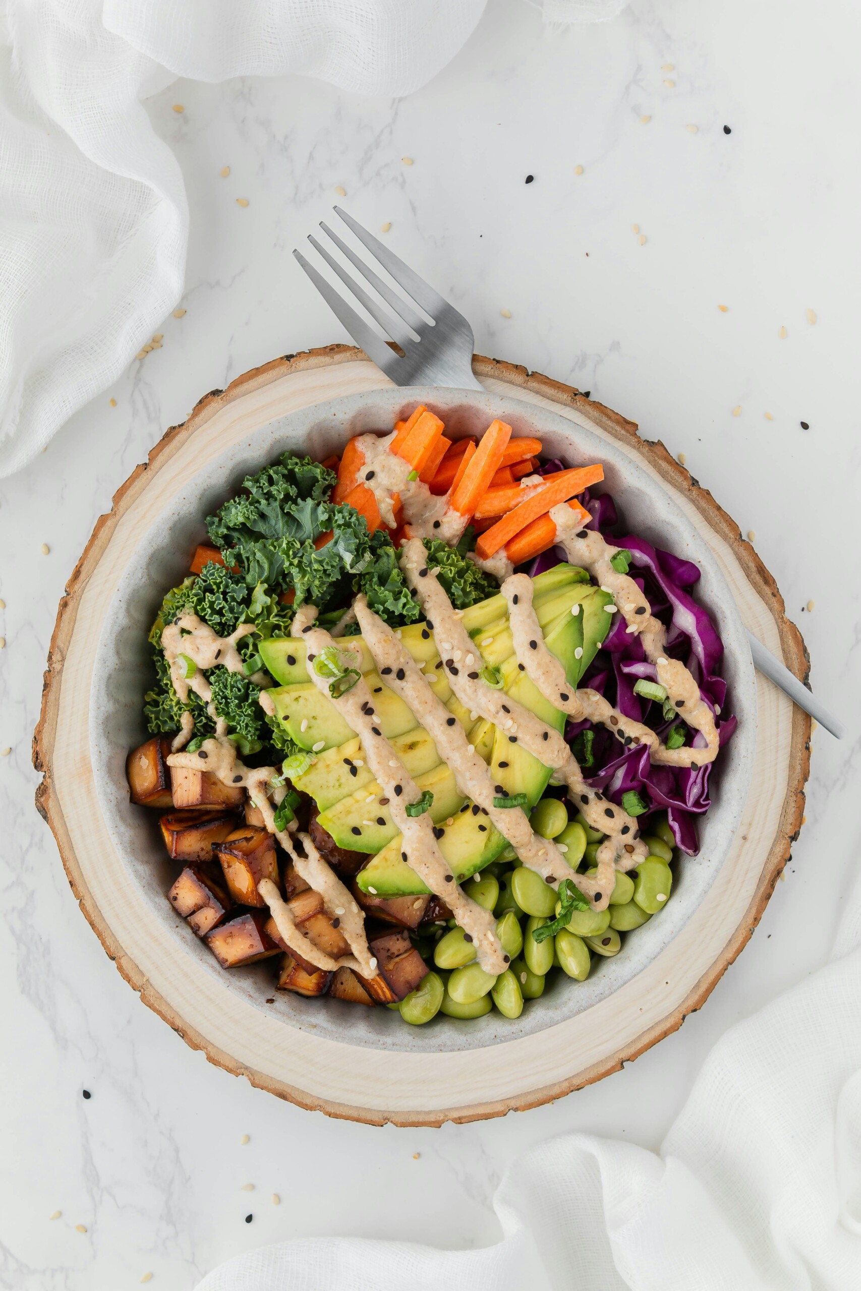 protein bowl with kale, chicken, avocado, carrots, edamame drizzeled with dressing and sesame seeds