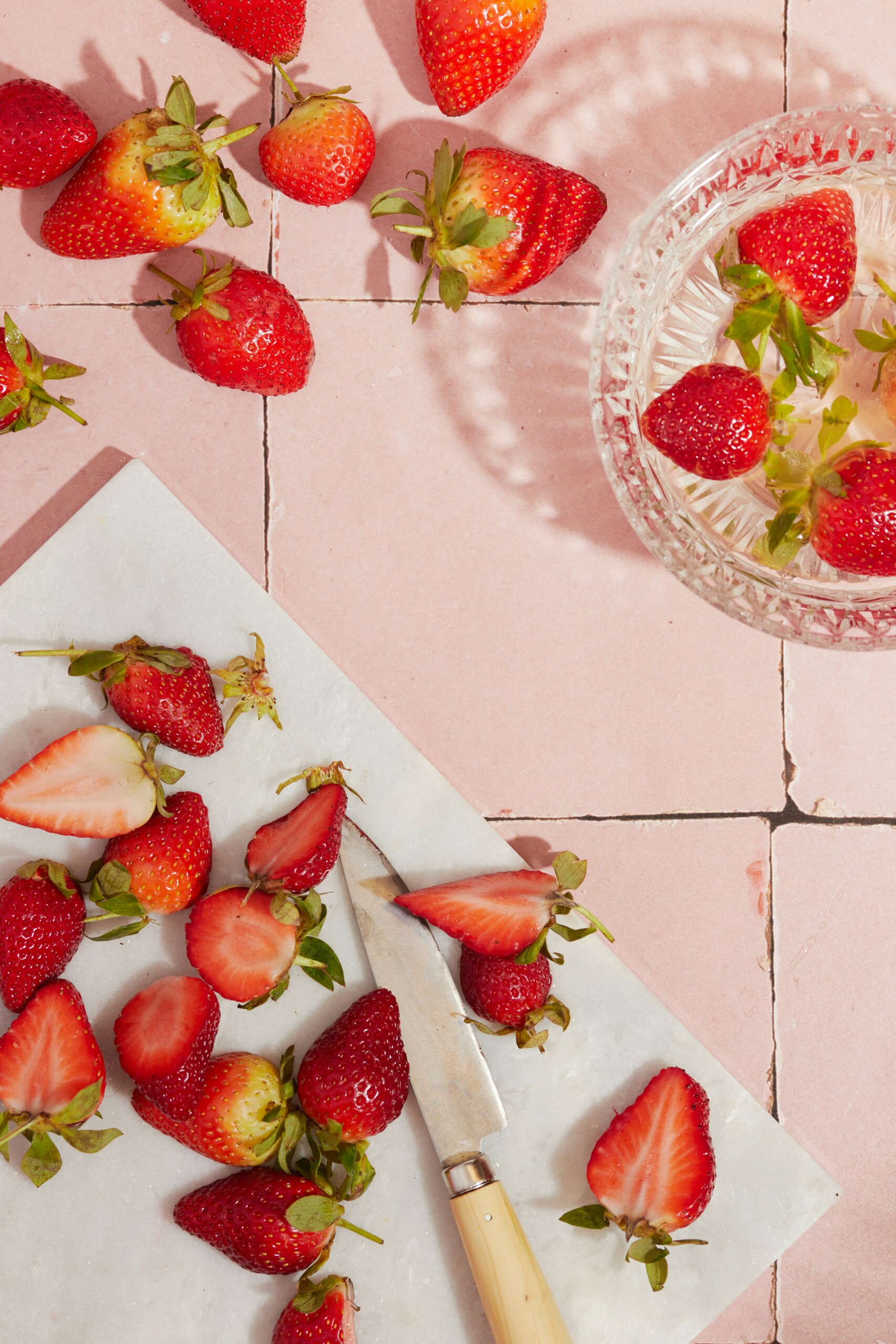 a cutting board with strawberries and glass dish