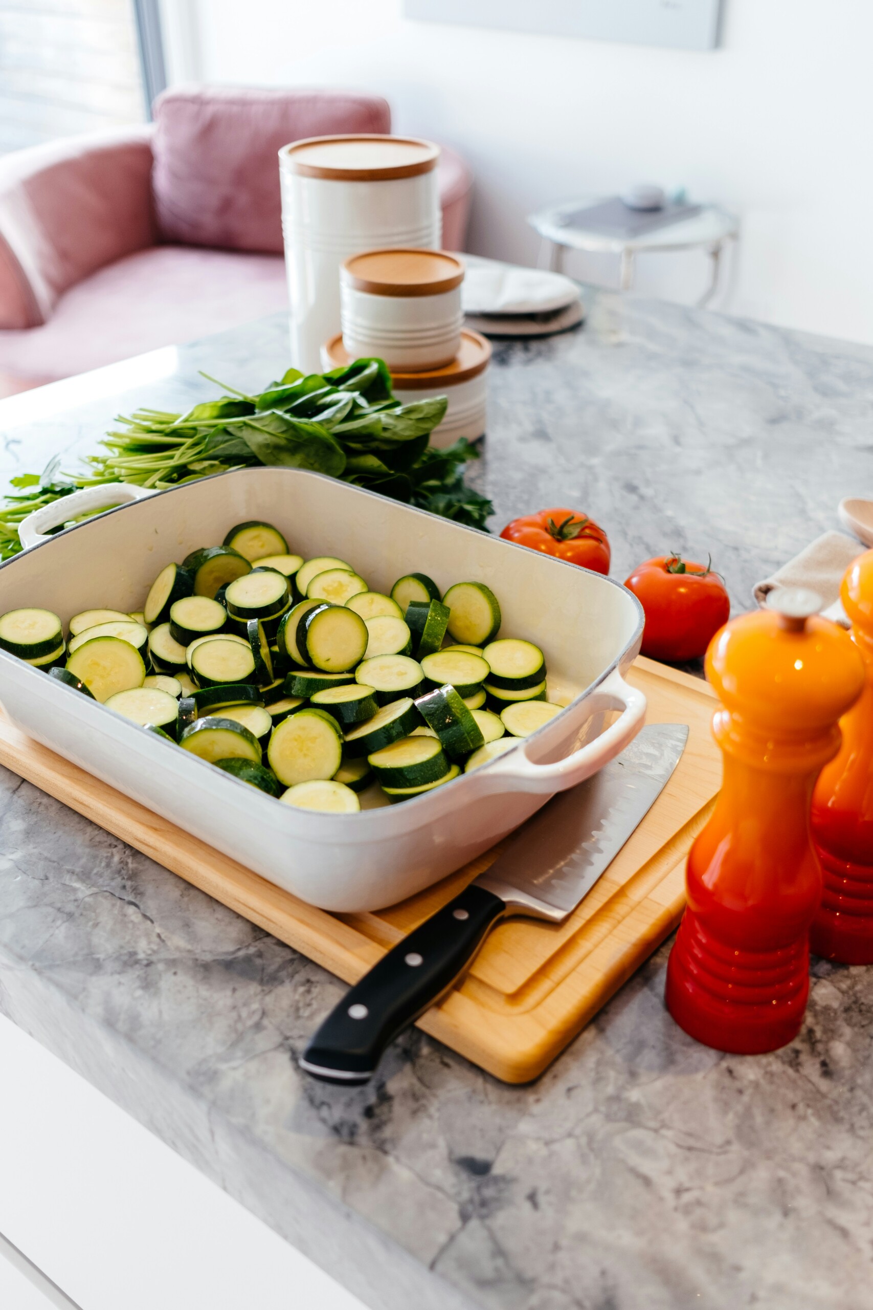 casserole dish on a cutting board with zuchini. peppers and salt shaker next to dish